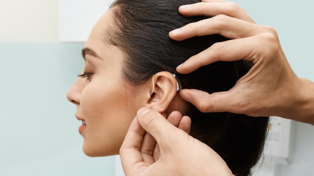 Audiologist fitting a receiver-in-canal hearing aid to a patient during a hearing aid fitting appointment