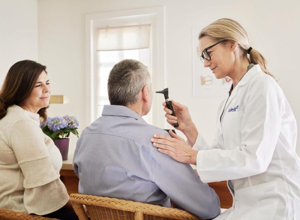 Audiologist using an otoscope to examine a patient ear canal before microsuction ear wax removal