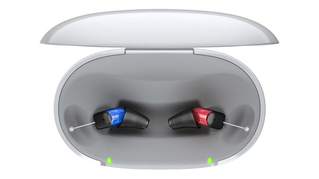 A pair of rechargeable hearing aids sitting in an open charging case with the charge light on